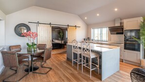 A modern kitchen with a central island, wooden flooring, and a sliding barn door leading to a bathroom. - Bearskin Cottage - Holiday At Home (Leyburn)