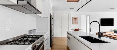 Une cuisine moderne avec des meubles blancs, une cuisinière en acier inoxydable et un plafond en bois.