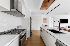 A modern kitchen with white cabinetry, a stainless steel stove, and a wooden ceiling.