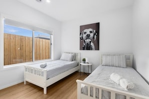 A bedroom with two beds, a window, and a wall-mounted dog painting.