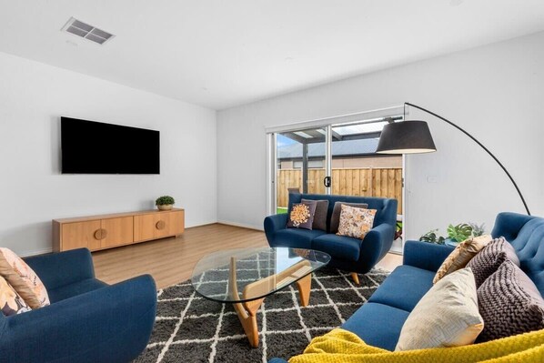 A modern living room with a blue sofa set, a glass coffee table, and a large black floor lamp.