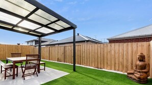 A patio with a table and chairs, a Buddha statue, and a wooden fence. - Halfway Gem - 3BR Home Between Geelong & The Coast (Mount Duneed)