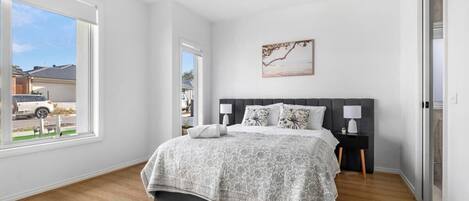 A bedroom with a large bed, two bedside tables, a window, and a painting on the wall.