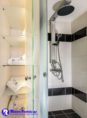 A modern bathroom with a glass shower enclosure, a handheld showerhead, and a towel rack with towels.