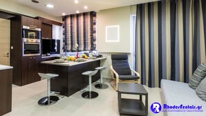 Een moderne keuken met inbouwapparatuur, een eetgedeelte met barstoelen en een woonruimte met een bank en gestreepte gordijnen.