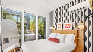 A modern bedroom with a large bed, a view of greenery outside, and a patterned wall. - Pool, Spa, FirePits, Speakeasy, Minigolf, Sleep 18 (Austin)