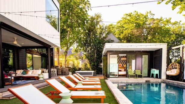 A modern outdoor pool area with lounge chairs, a small building with a sign, and a well-maintained lawn. - Pool, Spa, FirePits, Speakeasy, Minigolf, Sleep 18 (Austin)
