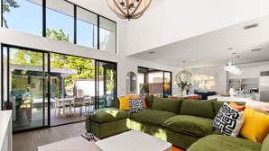 A spacious living area with a large green sofa, a white coffee table, and a glass door leading to an outdoor patio. - Pool, Spa, FirePits, Speakeasy, Minigolf, Sleep 18 (Austin)