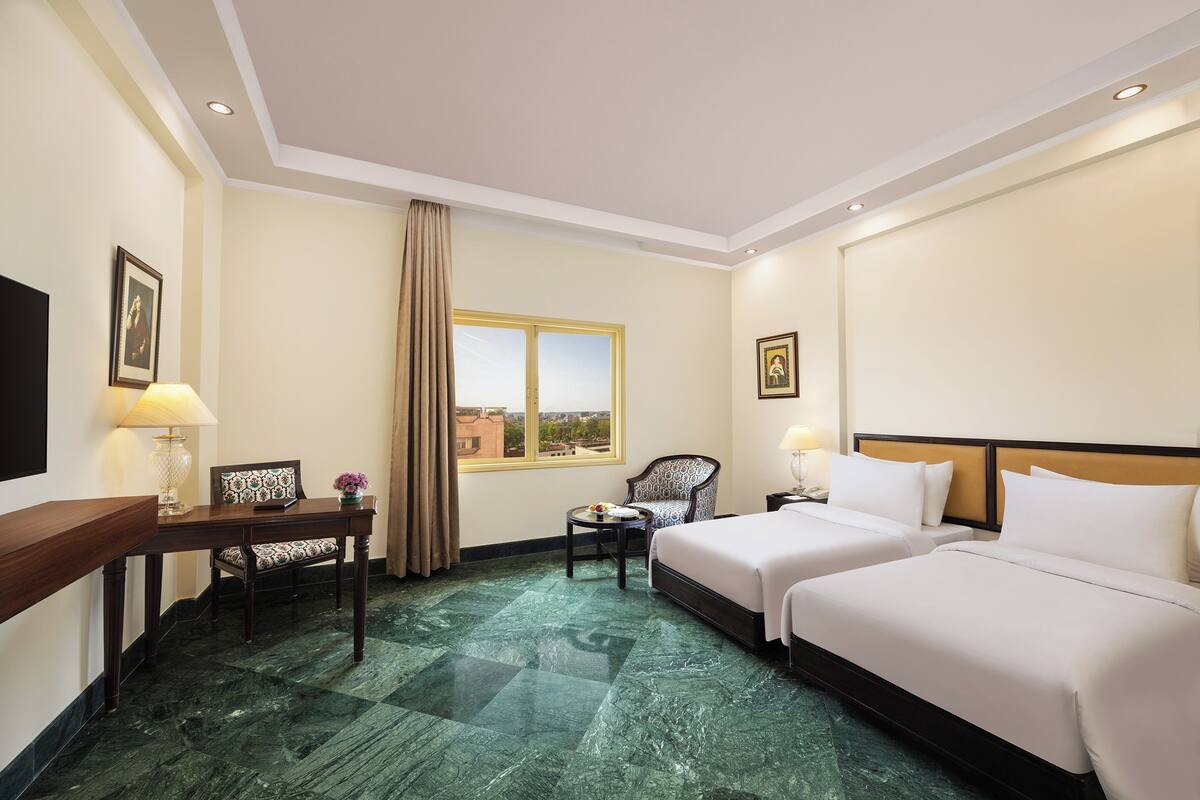 A hotel room with two beds, a desk with a chair, a window with a view, and a TV on the wall.