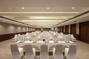 A large conference room with rows of white chairs and tables, equipped with name cards and floral centerpieces.