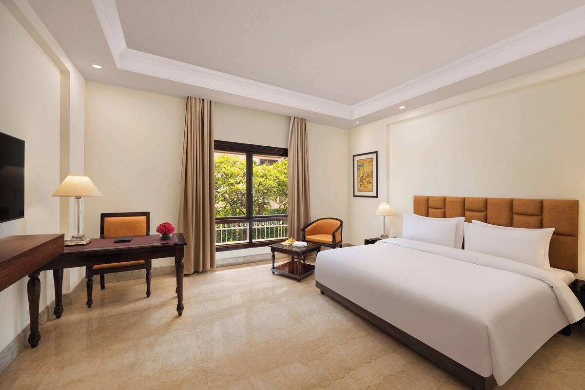 A hotel room with a large bed, a desk, a chair, a small table, and a window with curtains.