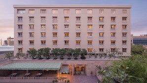 Un hotel de varios pisos con fachada plana, balcones y una terraza en la azotea con mobiliario.