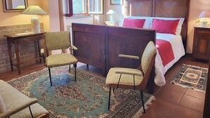 Een slaapkamer met een houten bed, twee stoelen, een bureau en een raam met gordijnen.