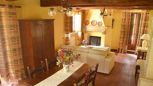 Un coin repas avec une table en bois, des chaises, un vase de fleurs, une cheminée et un canapé.