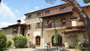 A stone building with a balcony, outdoor seating, and a large tree in front. - Casa Brina E: A characteristic and welcoming apartment that is part of an ancient country house made of stone, with Free WI-FI. (Monte Santa Maria Tiberina)