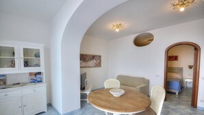 Un comedor con una mesa redonda de madera, sillas blancas, un aparador con puertas de vidrio y un cuadro en la pared.