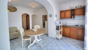 Cocina compacta con armarios de madera, encimera blanca y comedor con mesa redonda y sillas.