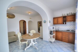 A compact kitchen with wooden cabinets, a white countertop, and a dining area with a round table and chairs.