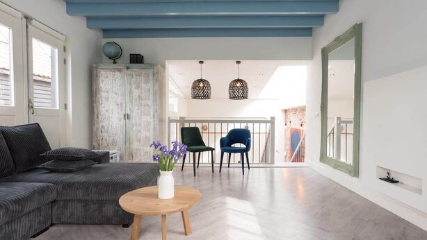 A spacious living area with a grey sectional sofa, a round wooden coffee table, and two chairs. A white vase with purple flowers is on the table. - Pakhuis aan de Zaan Wormerveer (Wormerveer)