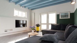 A modern living room with a sectional sofa, a flat-screen TV, and a round coffee table with decorative items. - Pakhuis aan de Zaan Wormerveer (Wormerveer)
