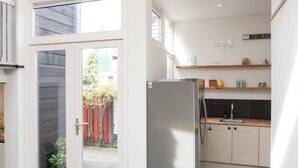 A modern kitchen with a stainless steel refrigerator, a dining area with a yellow table and a pink chair, and a large sliding glass door leading to a garden. - Pakhuis aan de Zaan Wormerveer (Wormerveer)