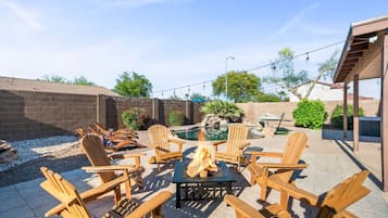 Un área de patio al aire libre con un brasero, sillas de madera y una piscina.