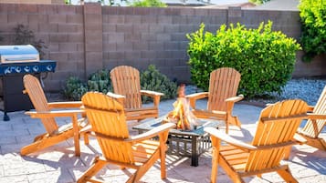A patio with wooden Adirondack chairs arranged around a fire pit.