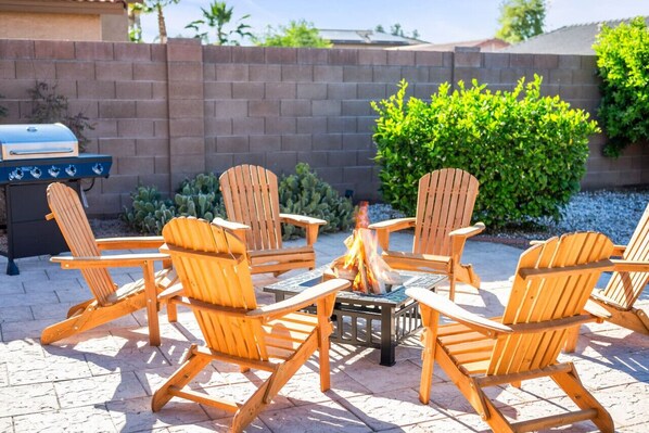 A patio with wooden Adirondack chairs arranged around a fire pit.