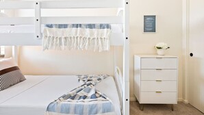 Ein Stockbett mit weißem Gestell, ein Nachttisch mit Schubladen und ein gerahmtes Zitat an der Wand.