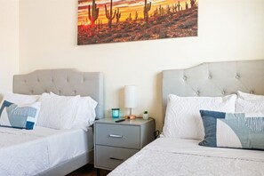 Una habitación de hotel con dos camas, una mesita de noche, una lámpara y un cuadro de un paisaje desértico en la pared.