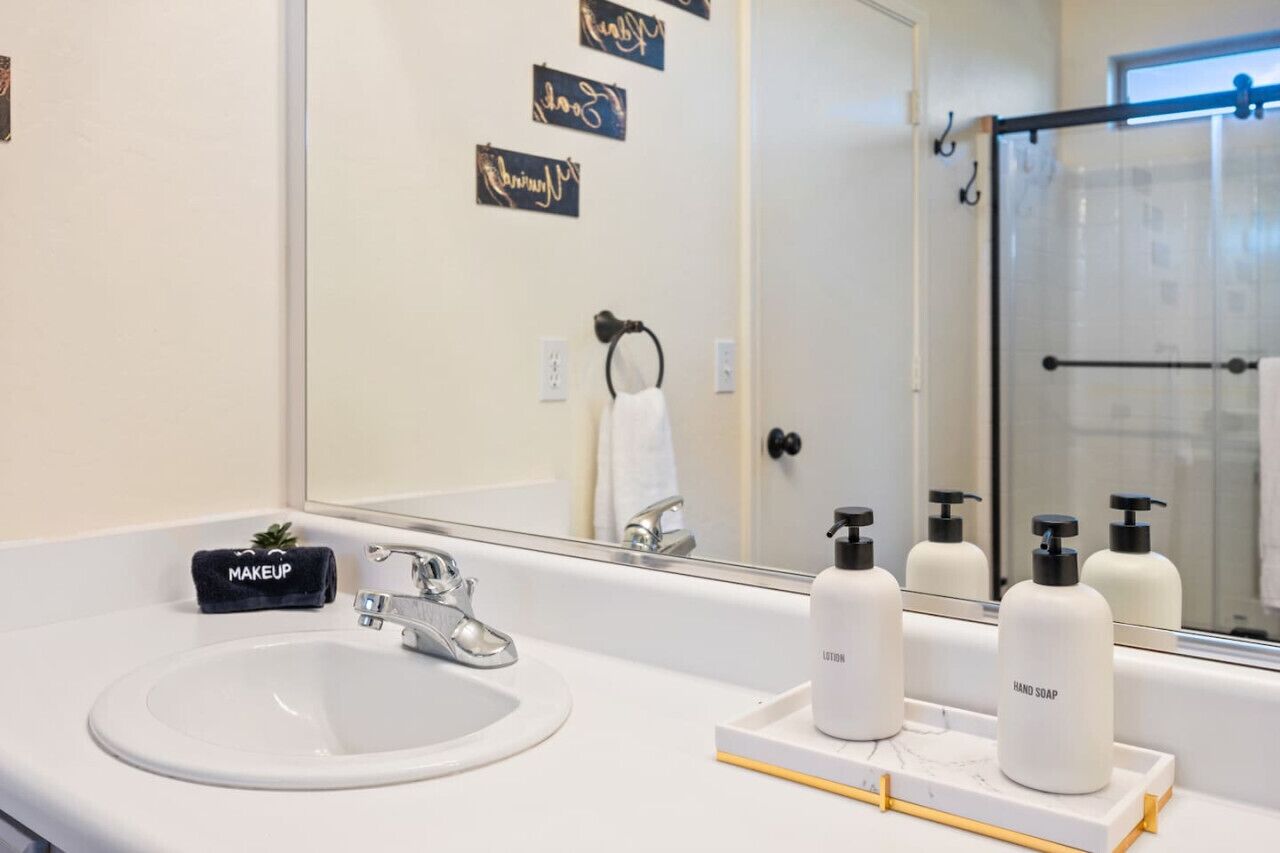 Et badeværelse med en hvid vask, et spejl og toiletartikler på bordet.