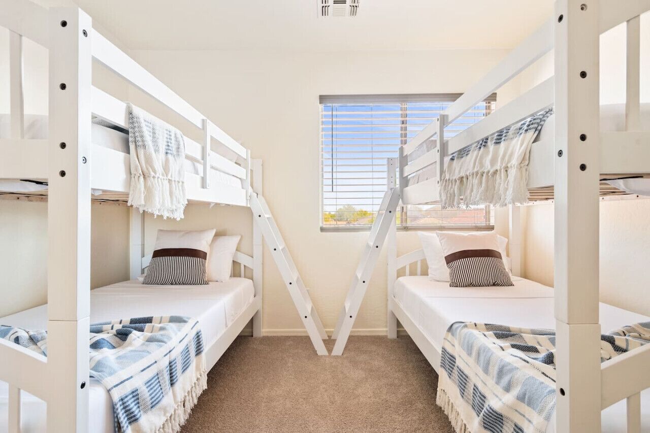 A room with bunk beds, a window with blinds, and a carpeted floor.