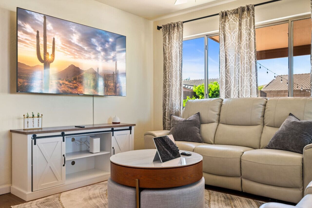 Una sala de estar con sofá, una mesa de centro, televisor montado en la pared y una ventana con cortinas.