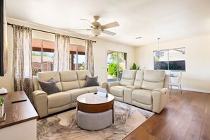 Ein geräumiges Wohnzimmer mit einem beigefarbenen Ecksofa, einem runden Couchtisch und einem Deckenventilator.