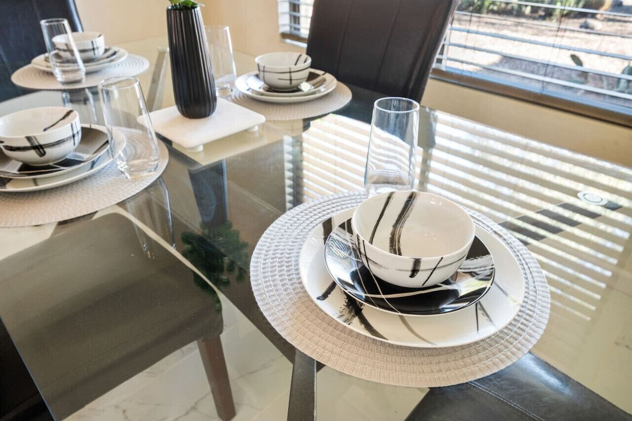 A dining table set with plates, bowls, and glasses, with a vase and a plant on the table.