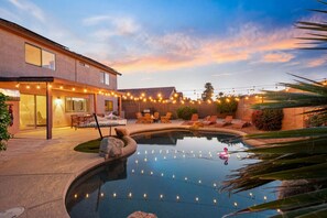 A pool area with a house, outdoor seating, and string lights.