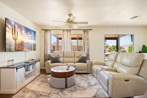 A living room with a sofa, a coffee table, a ceiling fan, and a large window with curtains.