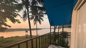 A balcony with a view of a lake, palm trees, and a blue awning. - Blue Lagoon Homestay (Mangaluru)