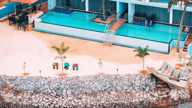 An aerial view of a resort with a swimming pool, palm trees, and beachside seating. - Blue Lagoon Homestay (Mangaluru)
