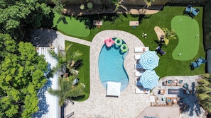 Vista aérea de un patio trasero con piscina, sillones de descanso y un pequeño campo de práctica de golf.