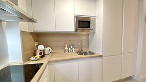 A modern kitchen with white cabinets, a stainless steel microwave, a kettle, and a sink. - Cozy Studio in Distrito Centro Malaga (Málaga)
