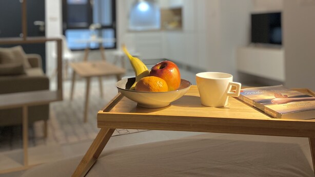 A modern living room with a wooden coffee table holding a bowl of fruit, a cup, and a book. - Cozy Studio in Distrito Centro Malaga (Málaga)