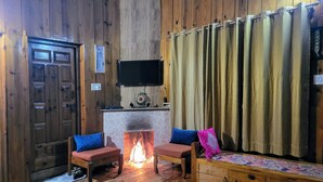 A cozy room with wooden walls, a fireplace, two chairs, a sofa, and a television mounted above the fireplace. - Hartola Panorama Cottage (Kosiyakutoli)