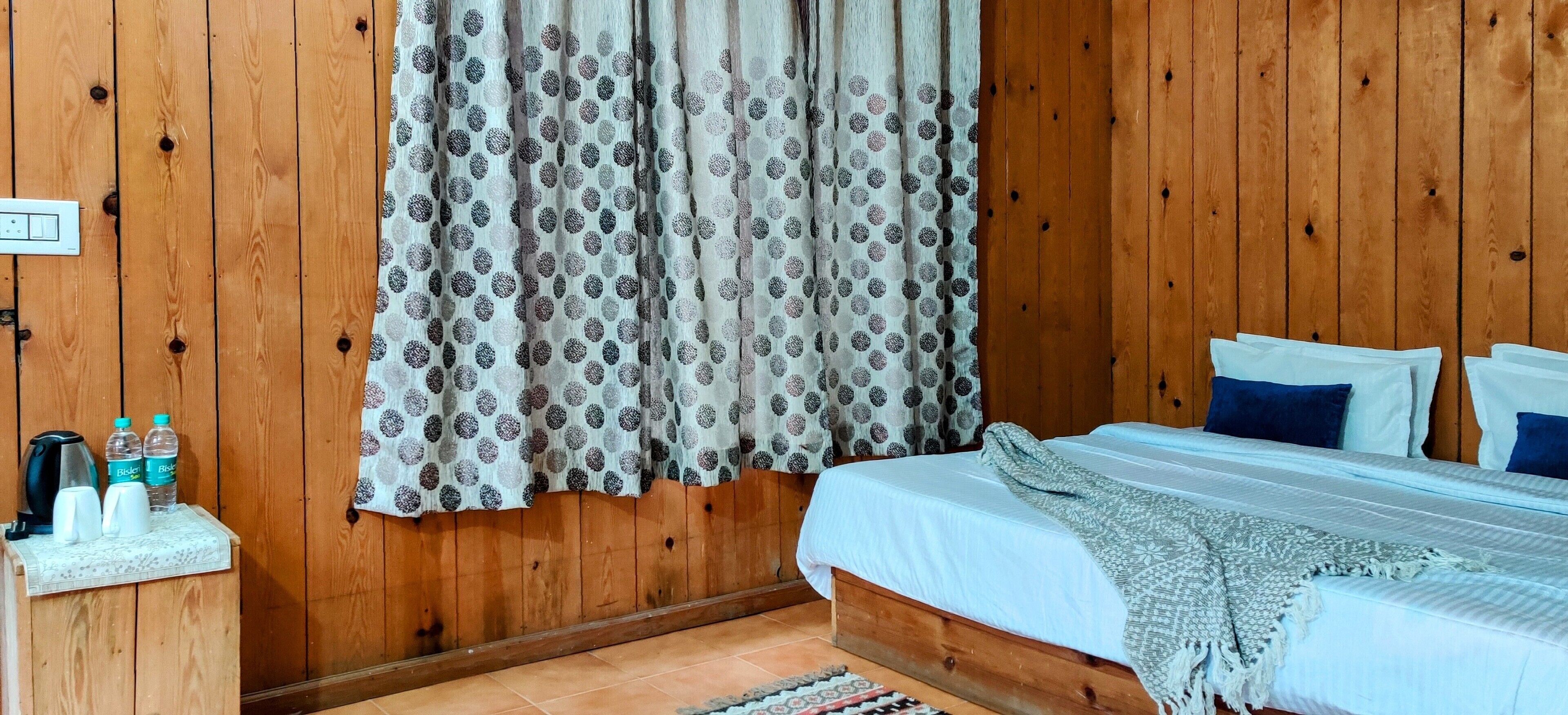A wooden-paneled room with a bed, a nightstand with a kettle, and a curtain with a polka dot pattern.