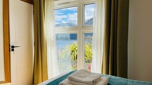 A hotel room with a bed, a window with curtains, and a view of greenery and mountains. - Avoca Lodge in the village of Onich (Fort William)