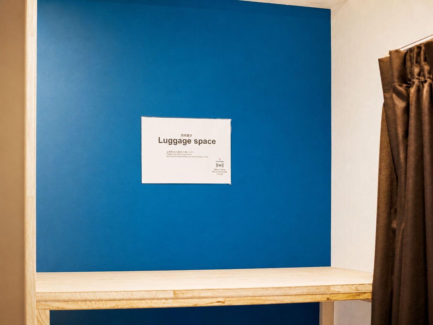 Un mur bleu sur lequel est affiché un panneau indiquant « espace pour les bagages », et une étagère en bois en dessous.