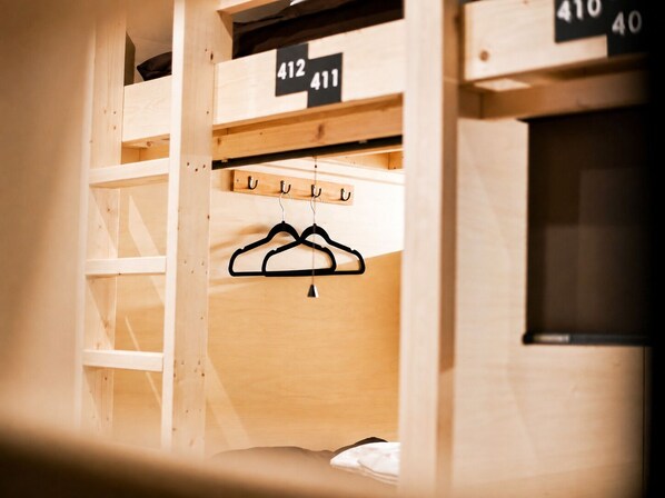 A wooden bunk bed with numbered compartments, a hanging rack with clothes, and a window.