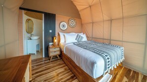 Een tent met een bed, nachtkastje, lamp en een spiegel.