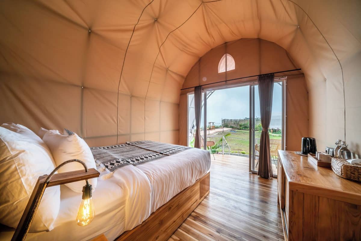 Een slaapkamer in tentstijl met een bed, een houten dressoir en uitzicht op de omgeving.