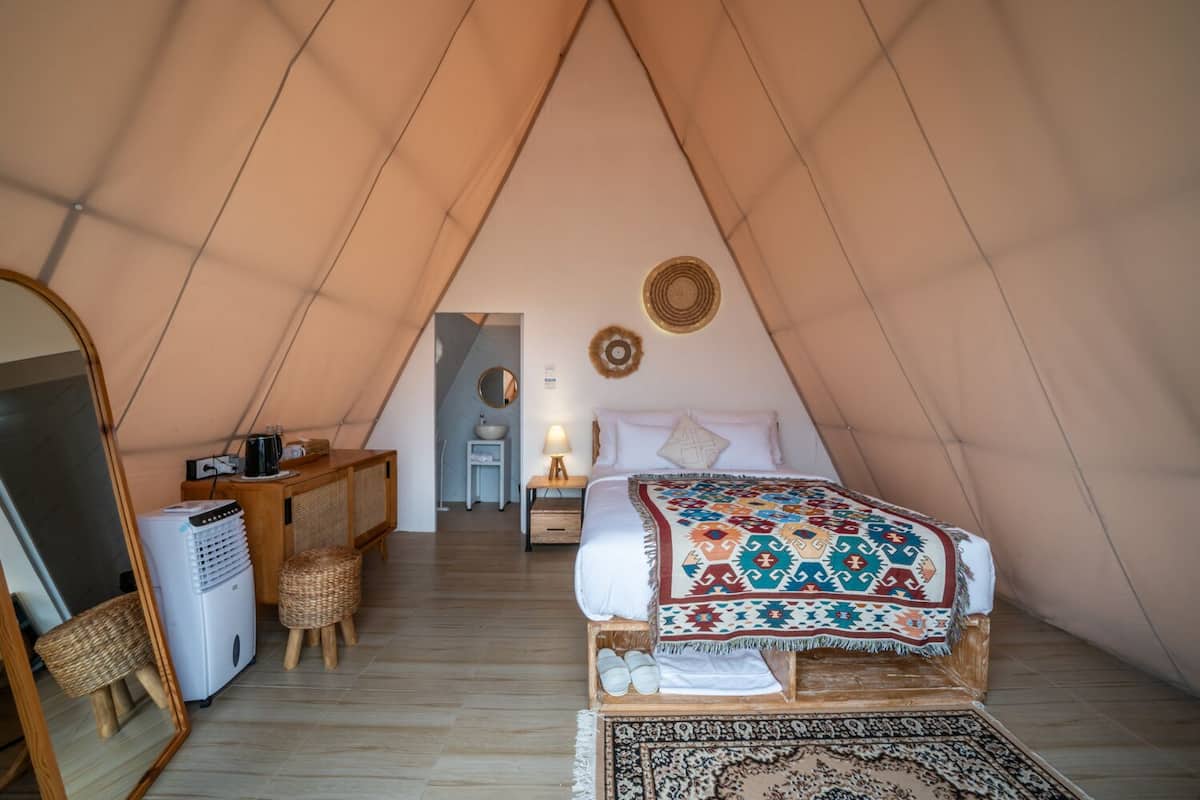 Een knus, driehoekig tentvormig vertrek met een bed, een klein bureau, een stoel, een spiegel en een wastafel.